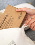 Person holding a cardboard box labeled 'Arrival & Diapering Kit' on a white surface.