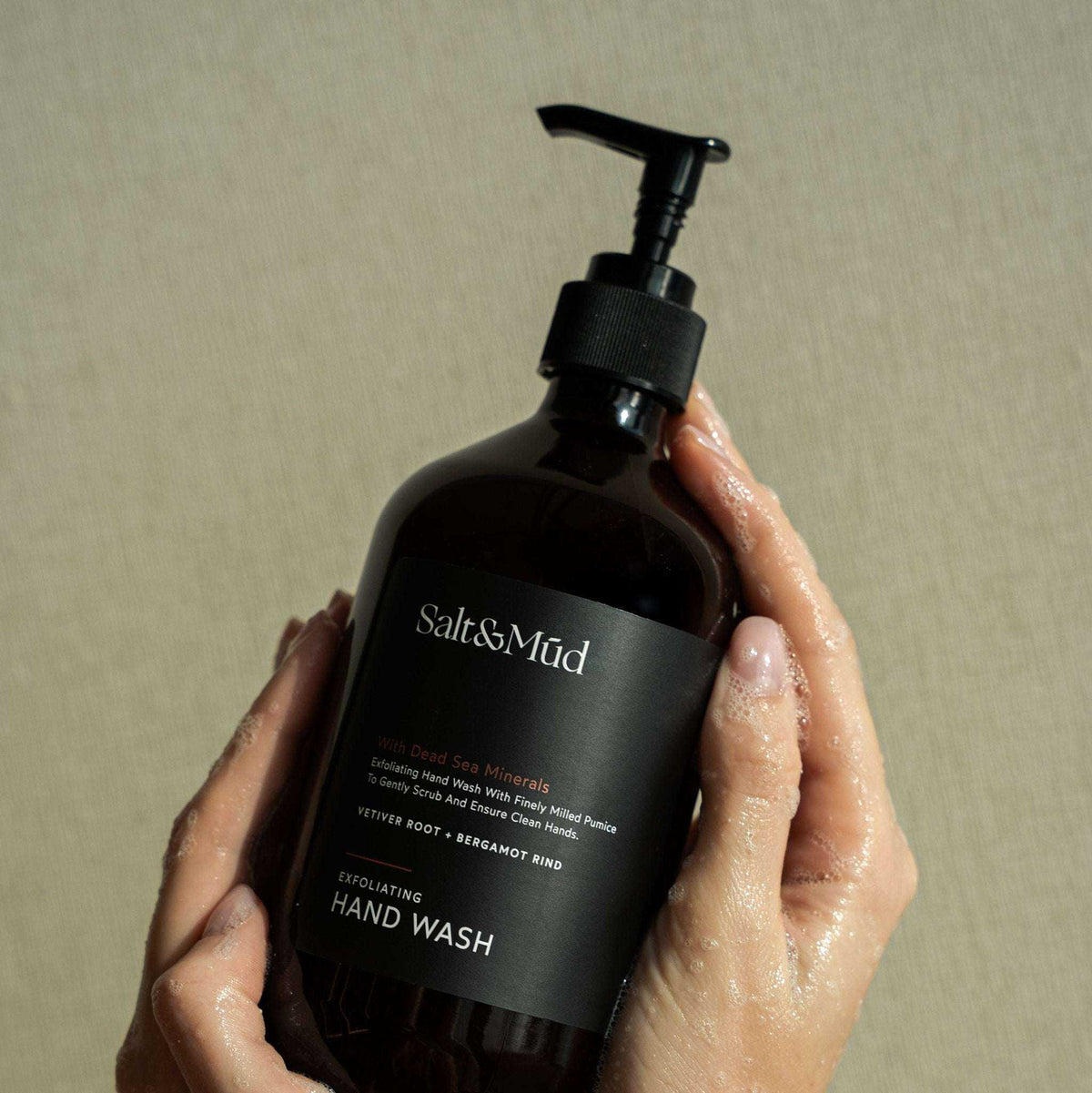 Wet hands holding a Salt & Mud Exfoliating Hand Wash amber bottle