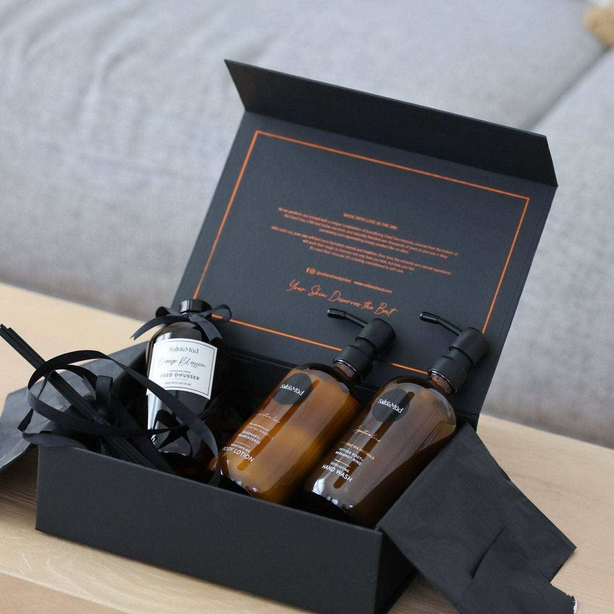 Luxury Hotel Amenities gift set with amber personal care bottles, black pumps, and a white-labeled bottle in a black box with orange trim.
